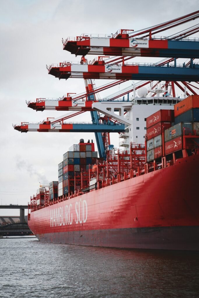 Red hull of a container ship beside port cranes